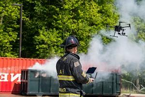 身着制服的消防员驾驶着无人机，背景是烟雾